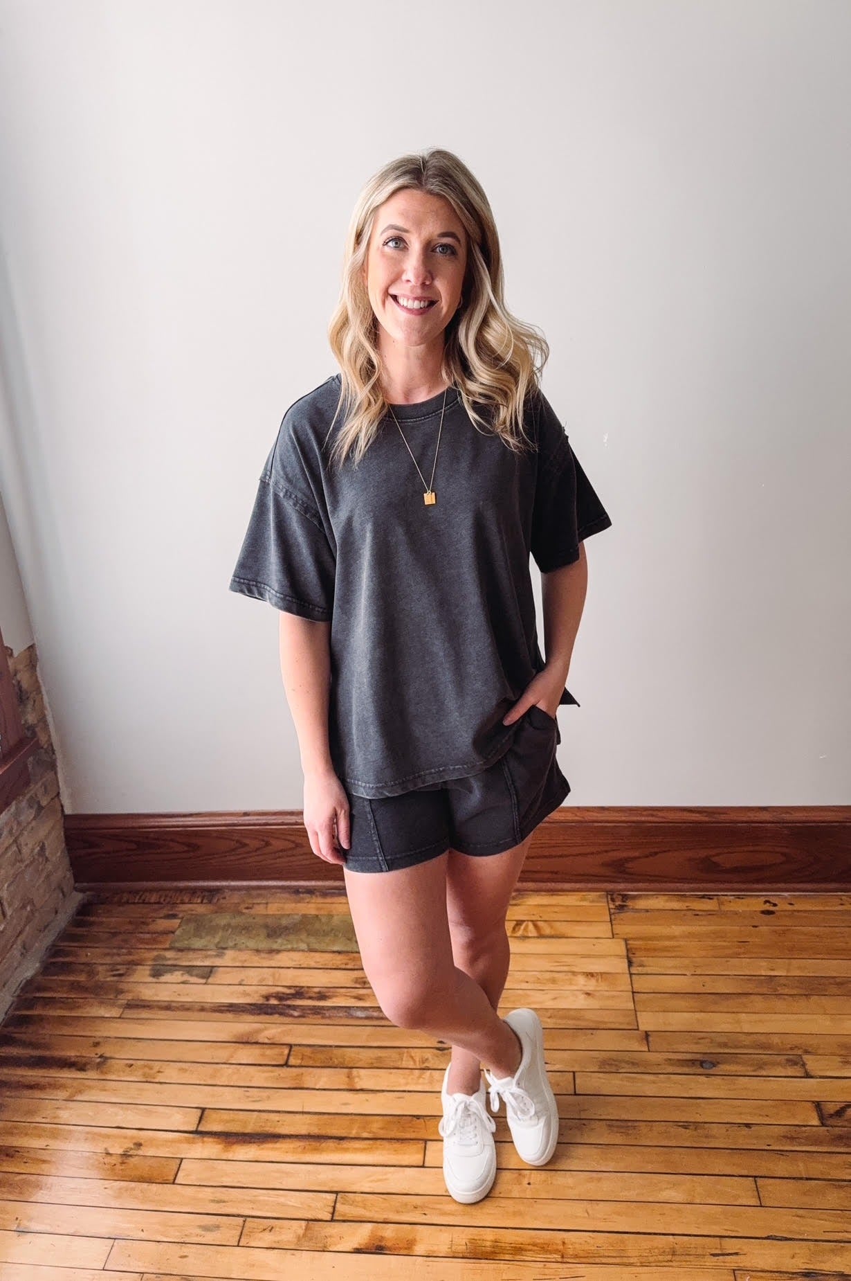 Woman wearing a dark gray t-shirt and shorts standing on a wooden floor.