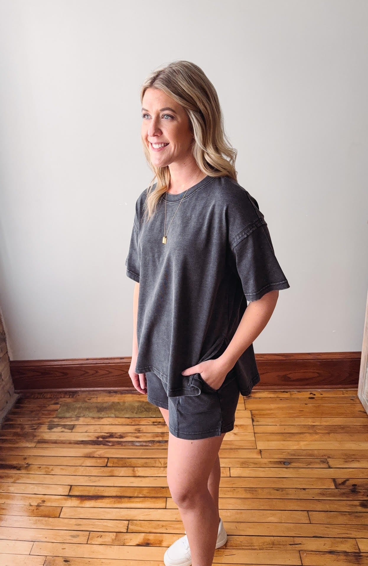 Woman wearing a gray oversized t-shirt and shorts standing in a room with wooden flooring.
