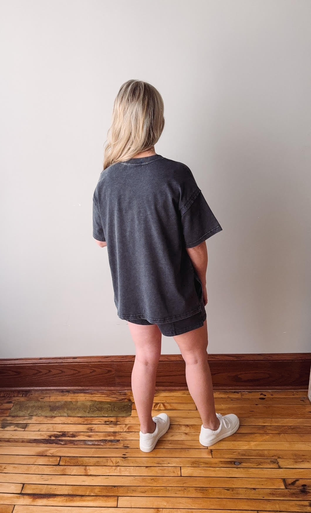 Person wearing a dark gray oversized t-shirt and shorts on a wooden floor.