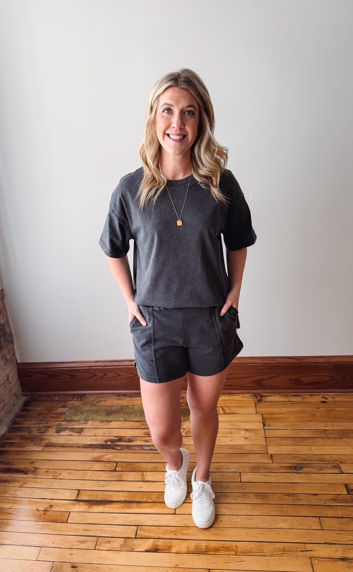 Woman wearing a gray t-shirt and shorts standing on a wooden floor.
