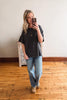 Woman taking a mirror selfie wearing a black t-shirt and blue jeans on a wooden floor.