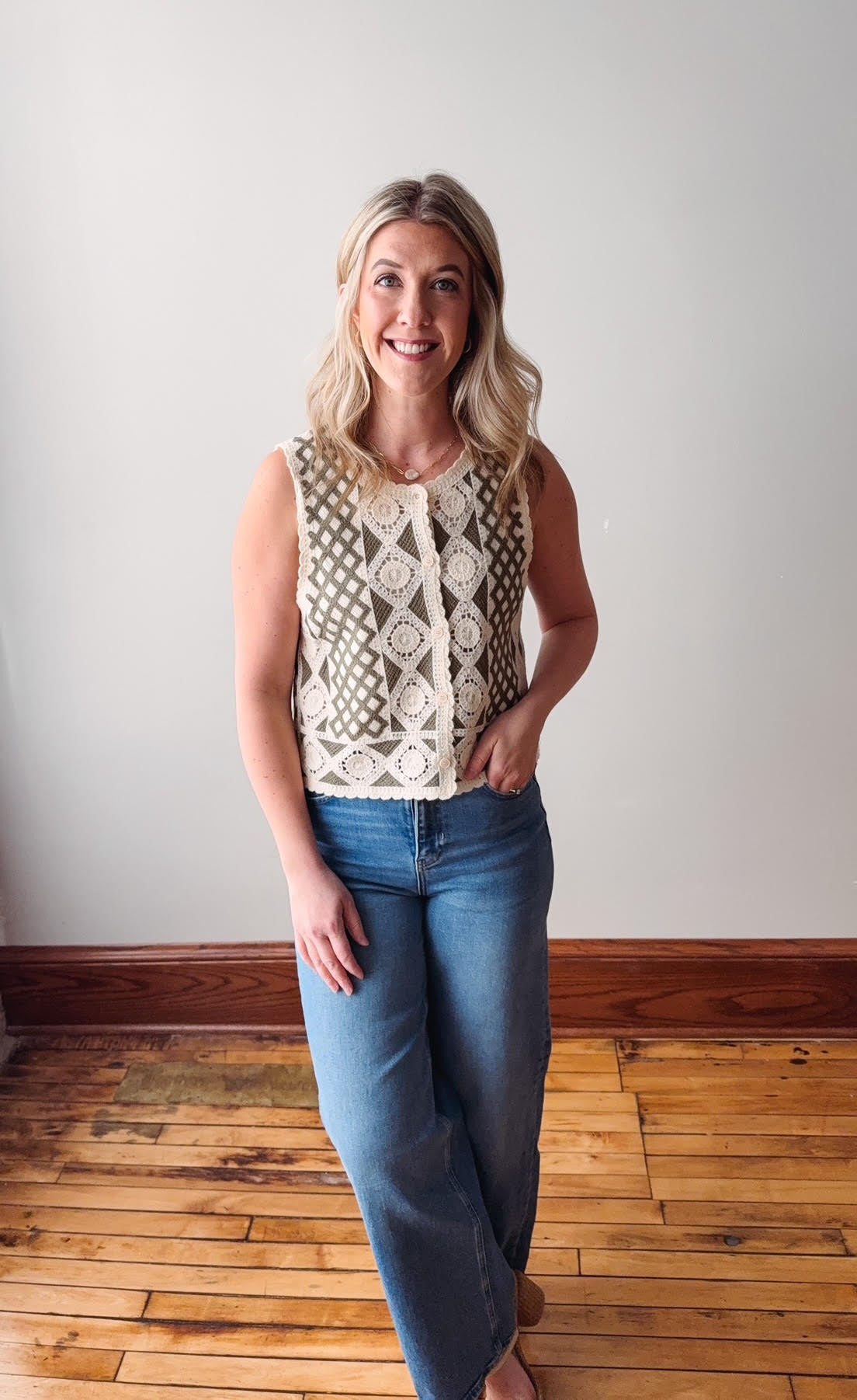 Woman wearing a sleeveless patterned top and blue jeans standing on a wooden floor.