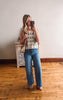 Woman taking a mirror selfie wearing a patterned top and blue jeans in a room with wooden flooring.