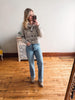 Woman taking a mirror selfie wearing a patterned sweater and jeans in a room with wooden flooring.