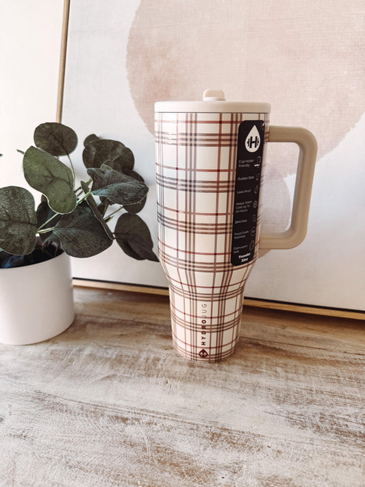 Plaid-patterned mug with a brand label on a wooden surface next to a plant