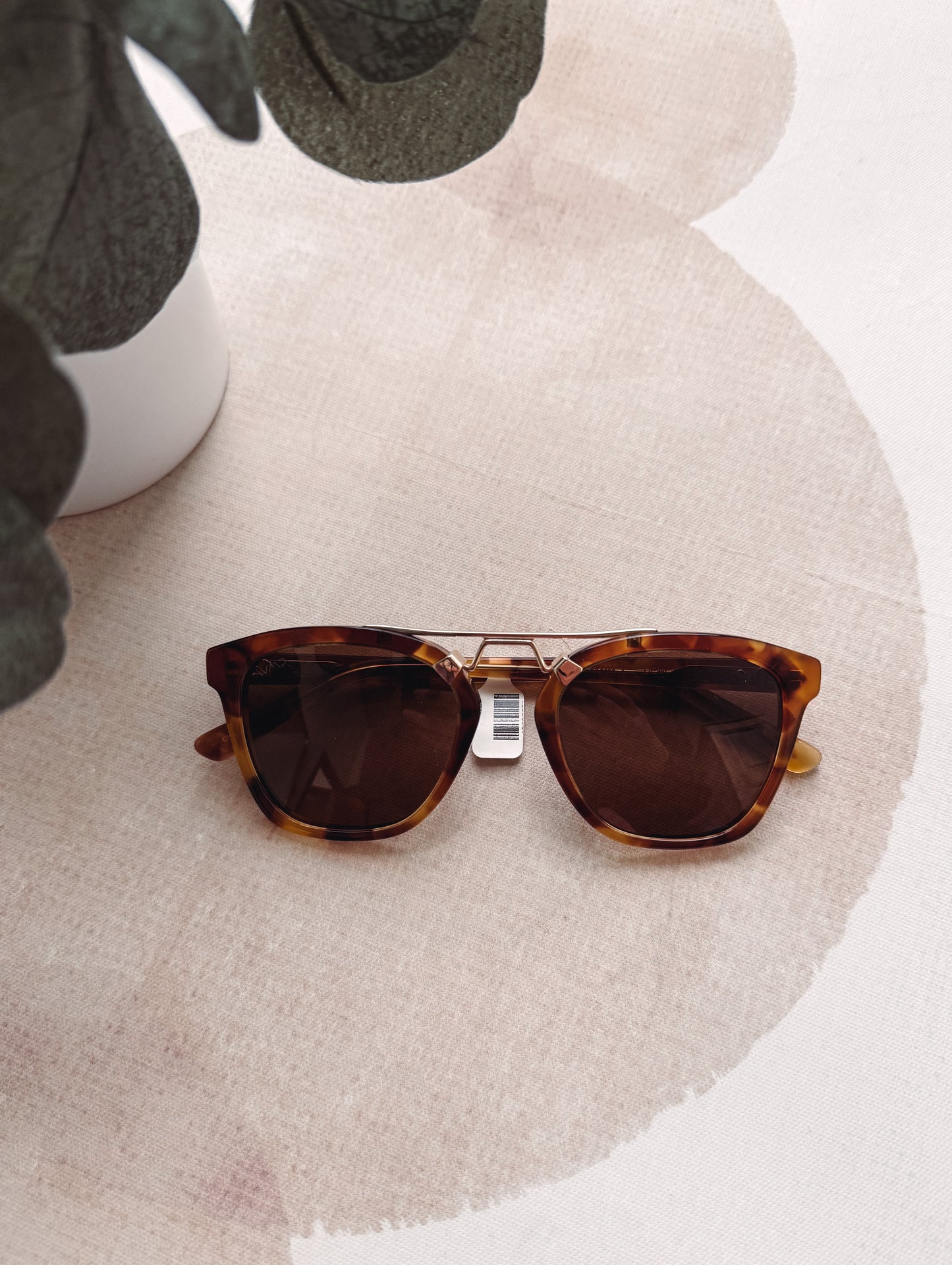 Tortoiseshell sunglasses with a tag on a textured beige surface