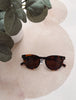 Tortoiseshell sunglasses on a beige cushion with a plant in the background
