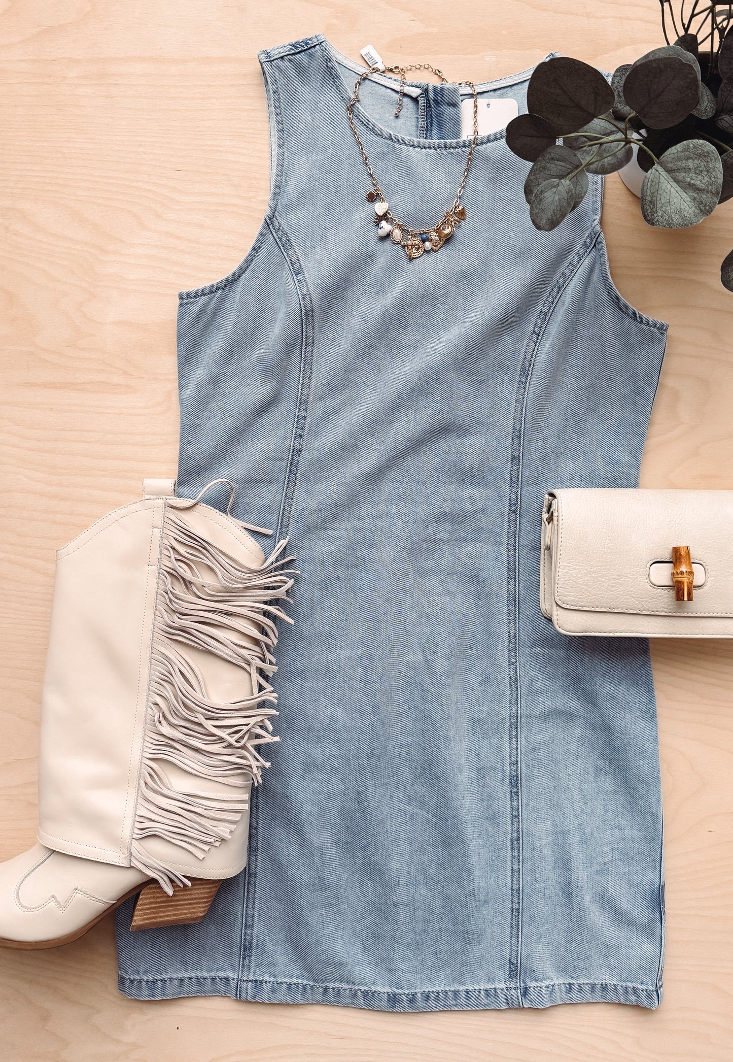 Denim dress with beige boot, handbag, and necklace on a wooden surface