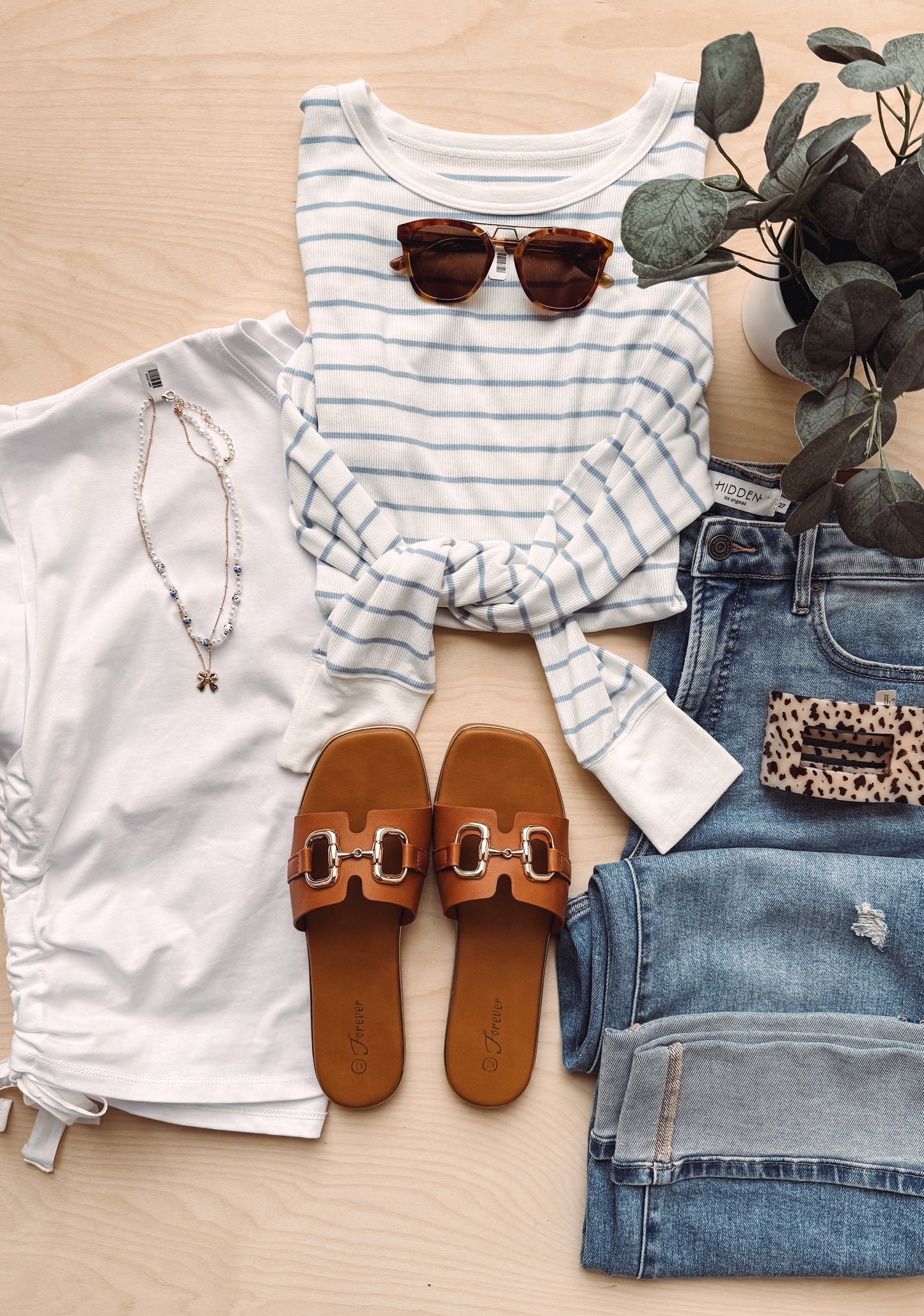 Fashionable outfit with striped shirt, jeans, sandals, and sunglasses on a wooden surface.