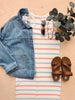 Denim jacket, striped shirt, sunglasses, necklace, and sandals on a wooden surface with eucalyptus leaves.