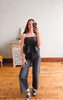 Woman taking a mirror selfie wearing a black polka dot top and gray pants in a room with wooden flooring.