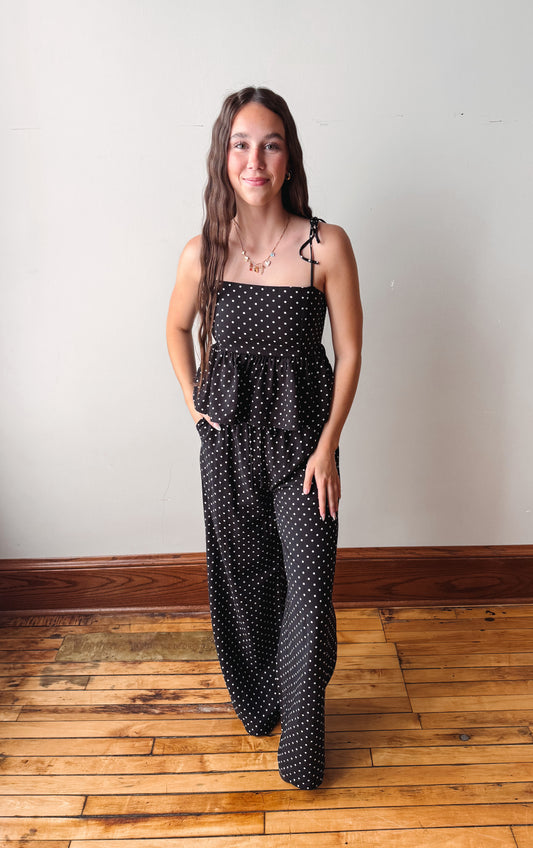 Woman wearing a black polka dot dress standing on a wooden floor with a white wall background