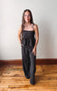Woman wearing a black polka dot dress standing on a wooden floor with a white wall background