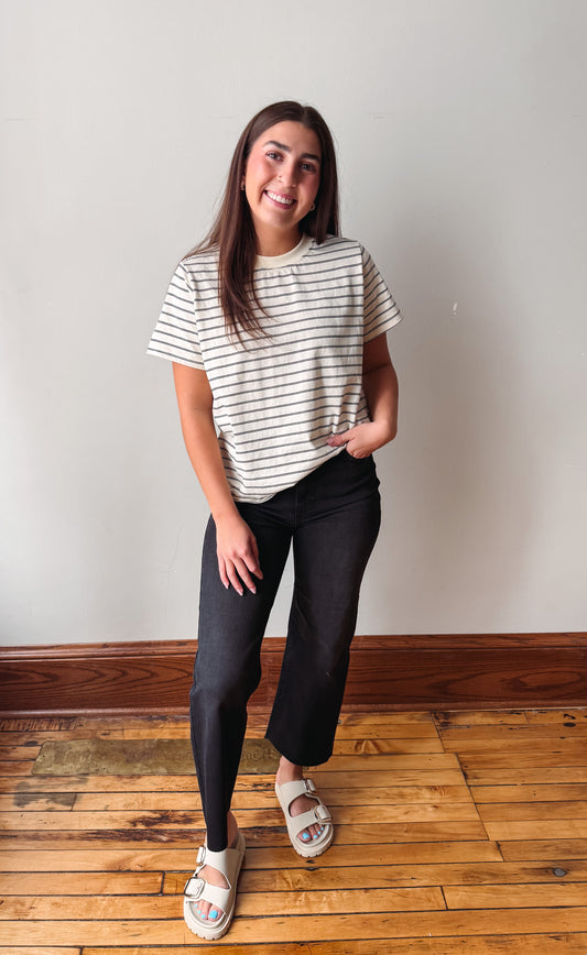Girl smiling wearing an ivory shirt withe black jeans against a plain wall.