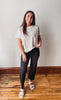 Girl smiling wearing an ivory shirt withe black jeans against a plain wall.