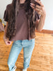 A person taking a mirror selfie wearing a brown short-sleeve t-shirt and light blue jeans on a wooden floor.