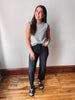 A woman modeling a sleeveless gray and white striped crop top with black cropped jeans and black slide sandals, standing on a wooden floor against a plain off-white wall.