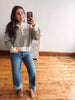 A woman takes a mirror selfie wearing a cream and navy striped long-sleeve henley sweater, blue cuffed jeans, and tan slide sandals in a room with light wood floors and a white wall.