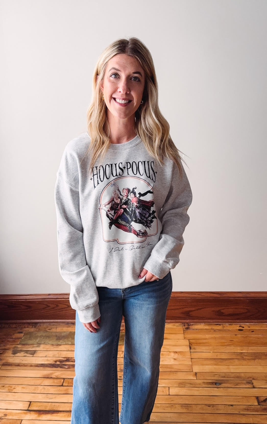 Woman wearing a 'Hocus Pocus' sweatshirt and jeans indoors.