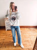 Woman taking a mirror selfie wearing a graphic sweatshirt and jeans in a room with wooden flooring.