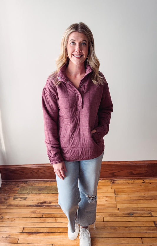 Woman wearing a purple quilted jacket and light blue jeans standing on a wooden floor.
