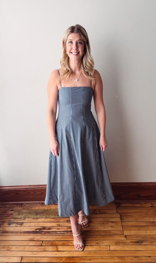 Woman wearing a strapless blue dress standing on a wooden floor with a white wall background