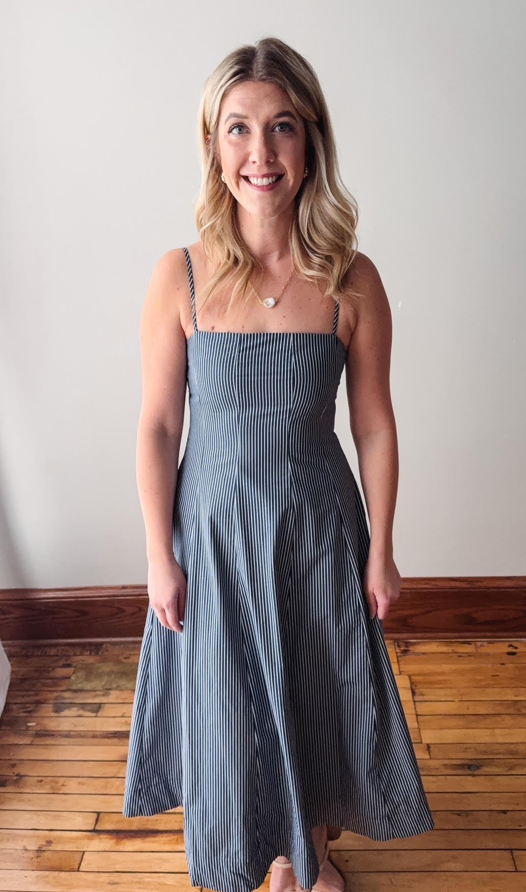 Woman wearing a blue dress standing on a wooden floor with a white wall background