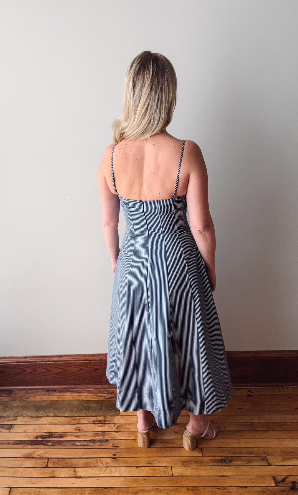 Woman wearing a blue dress standing on a wooden floor with a plain wall background