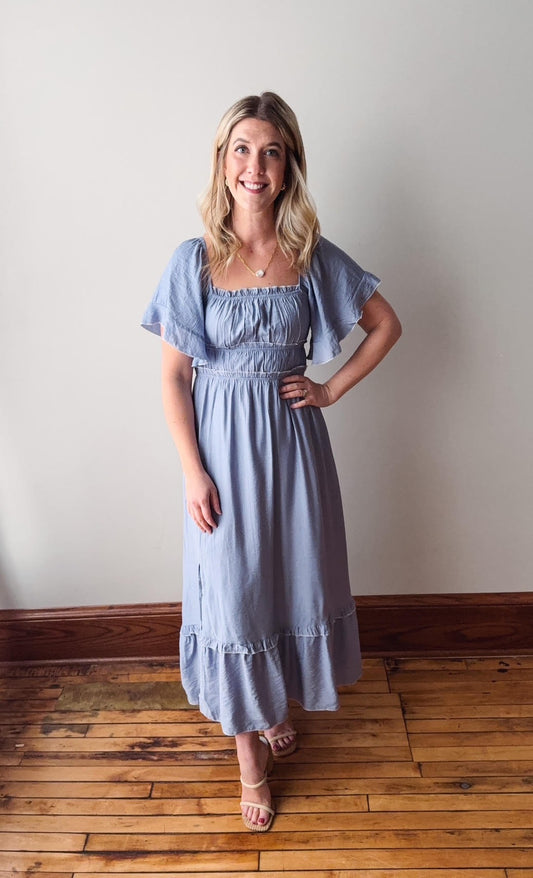 Woman wearing a light blue dress standing on a wooden floor with a white wall background
