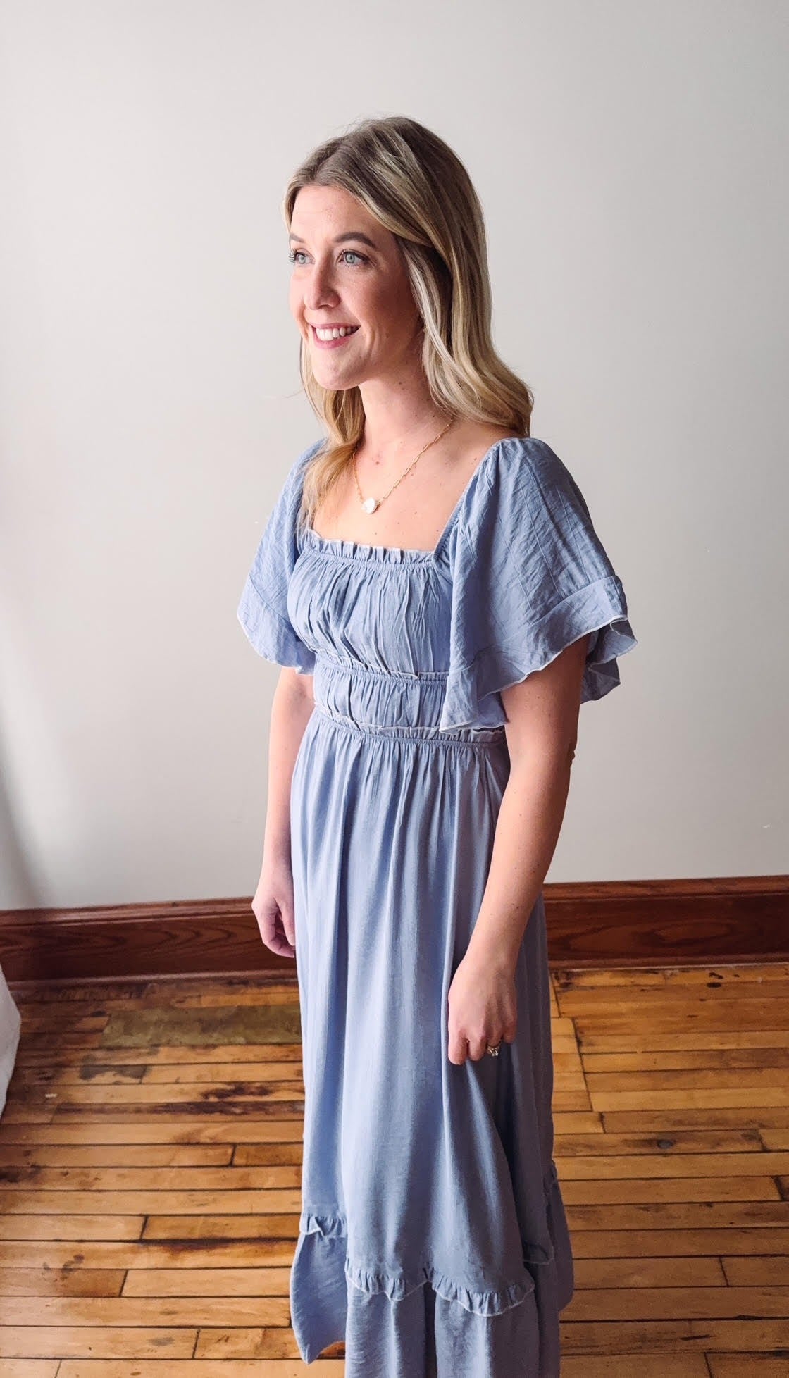 Woman wearing a light blue dress standing on a wooden floor with a white wall background