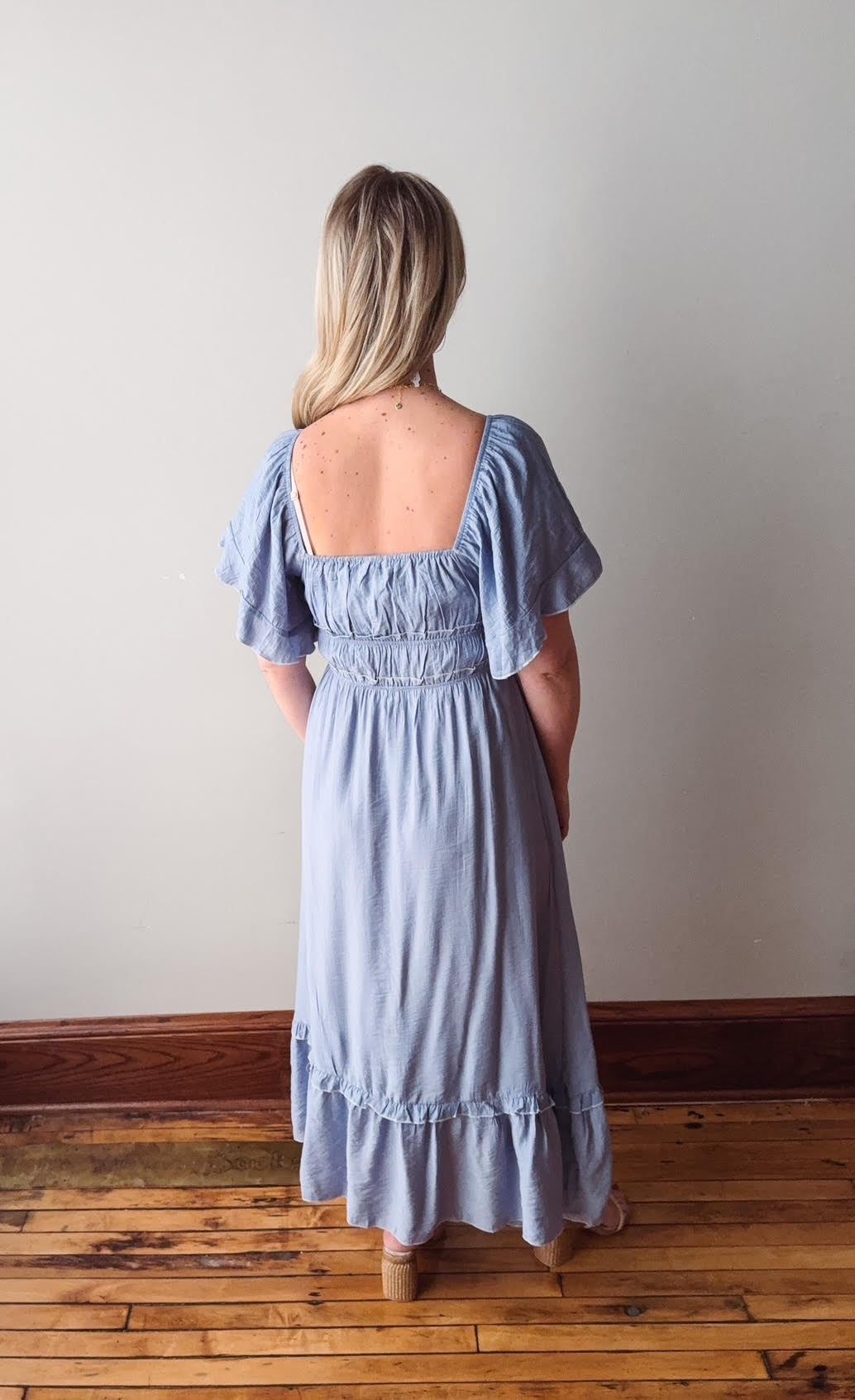Woman wearing a light blue dress standing on a wooden floor with a white wall background