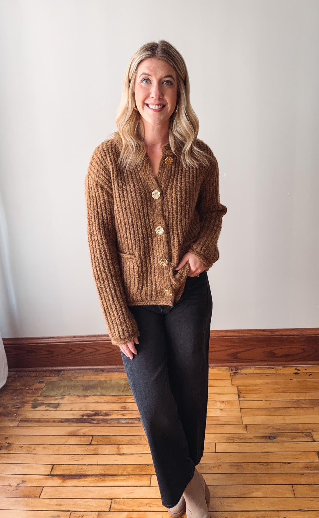 Woman wearing a brown knitted cardigan standing on a wooden floor.