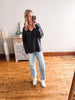 Woman taking a mirror selfie wearing a black sweater and light blue jeans in a room with wooden flooring.