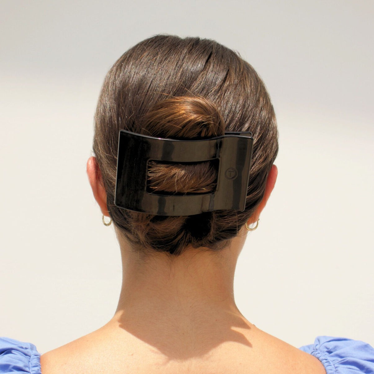 Person with a black hair clip in their bun against a plain background