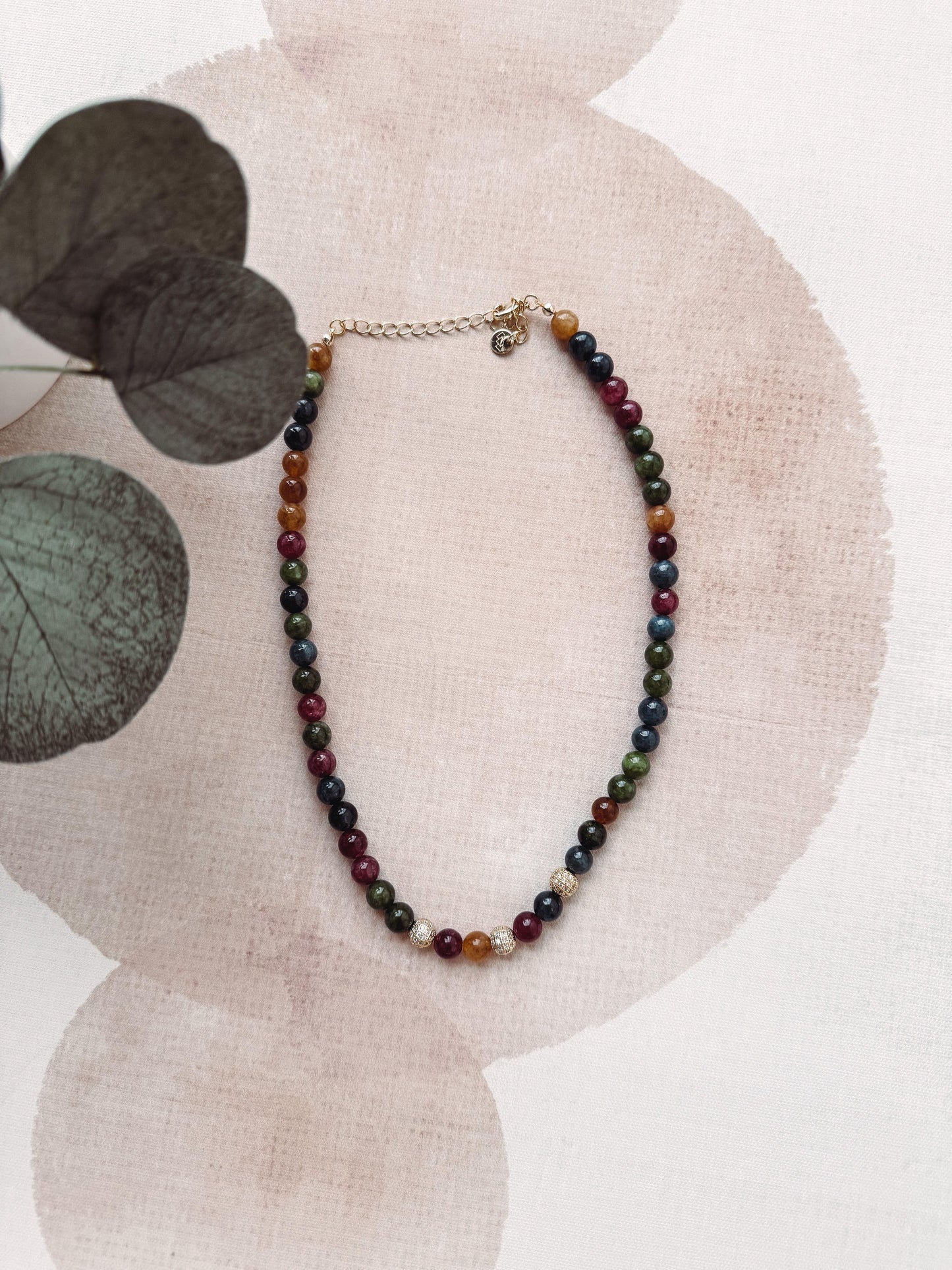 Multicolored beaded necklace on a white background with decorative leaves.