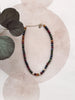 Multicolored beaded necklace on a white background with decorative leaves.