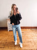 Woman taking a mirror selfie wearing a black jacket, light blue jeans, and white sneakers in a room with wooden flooring.
