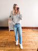 Woman taking a mirror selfie wearing a gray sweater, blue jeans, and white sneakers in a room with wooden flooring.