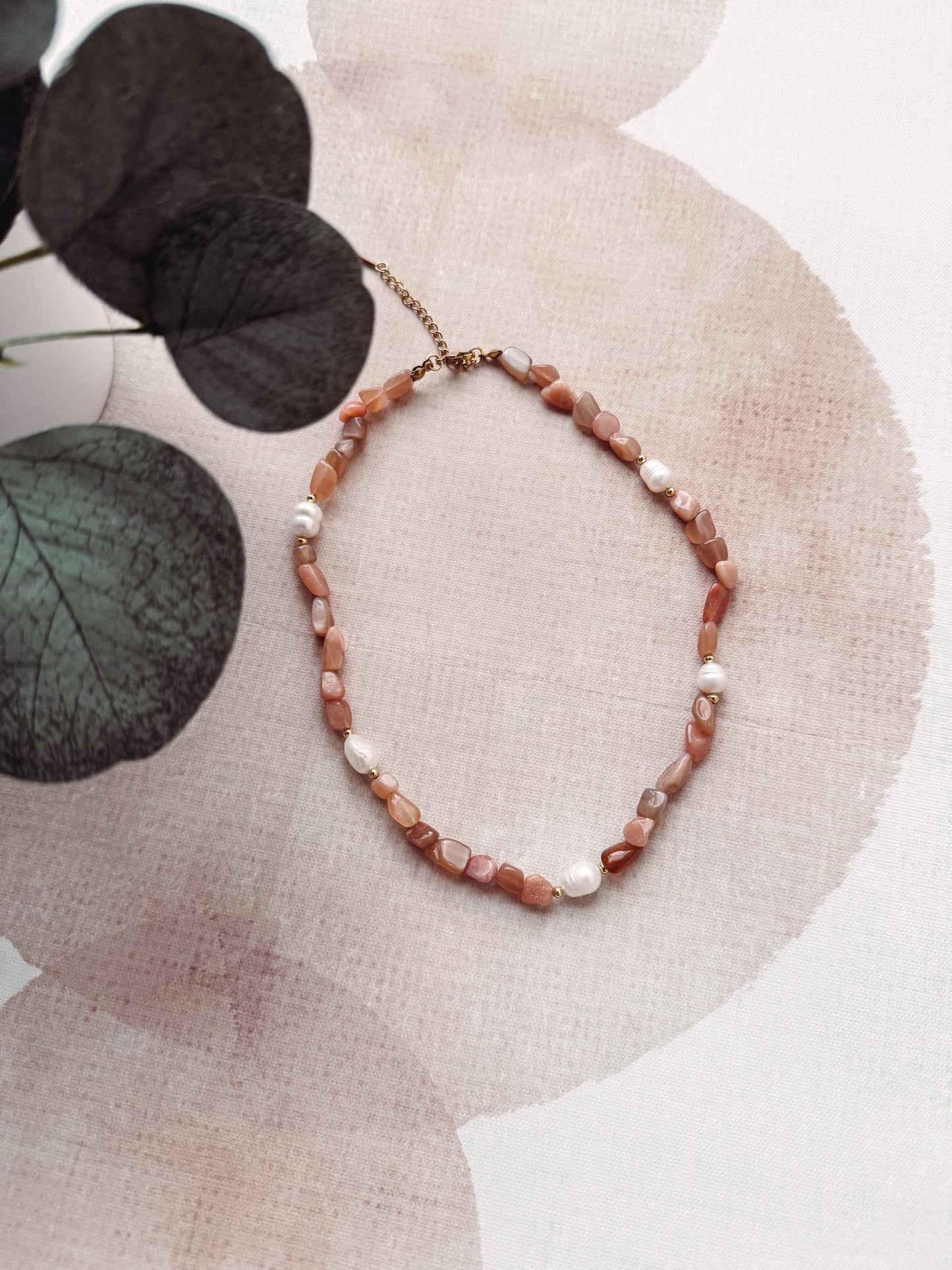 Necklace with brown and white beads on a textured surface with leaves