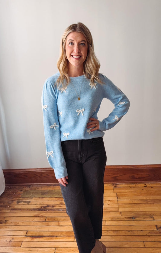 Woman wearing a light blue sweater with white floral patterns on a wooden floor.