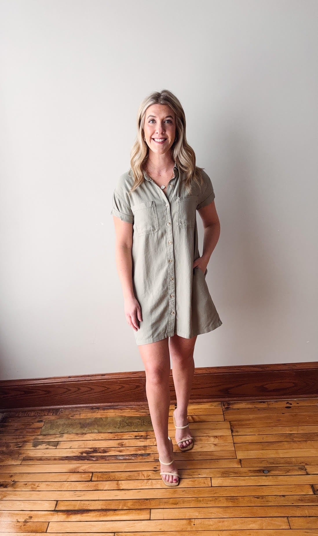 Woman wearing a green dress standing on a wooden floor with a white wall background