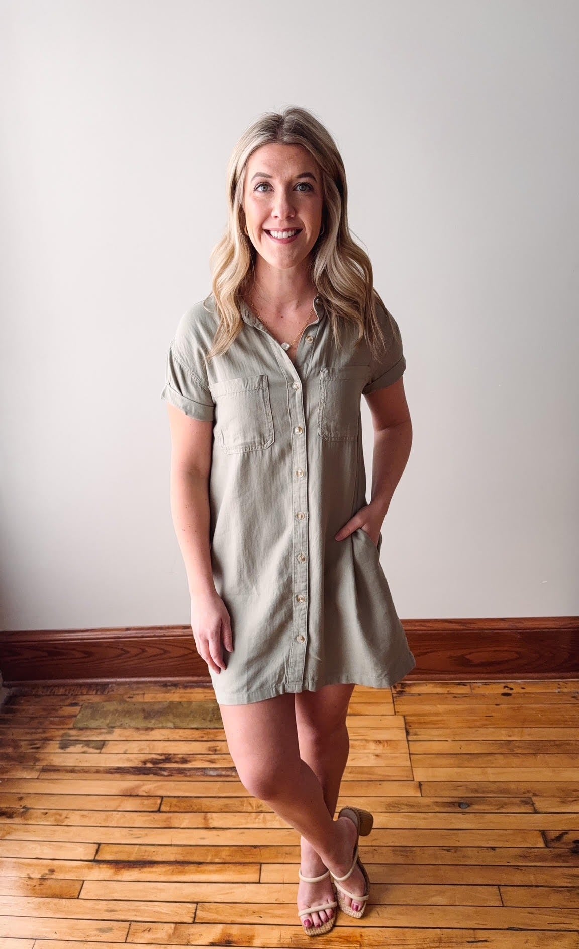 Woman wearing a light green dress standing on a wooden floor with a white wall background