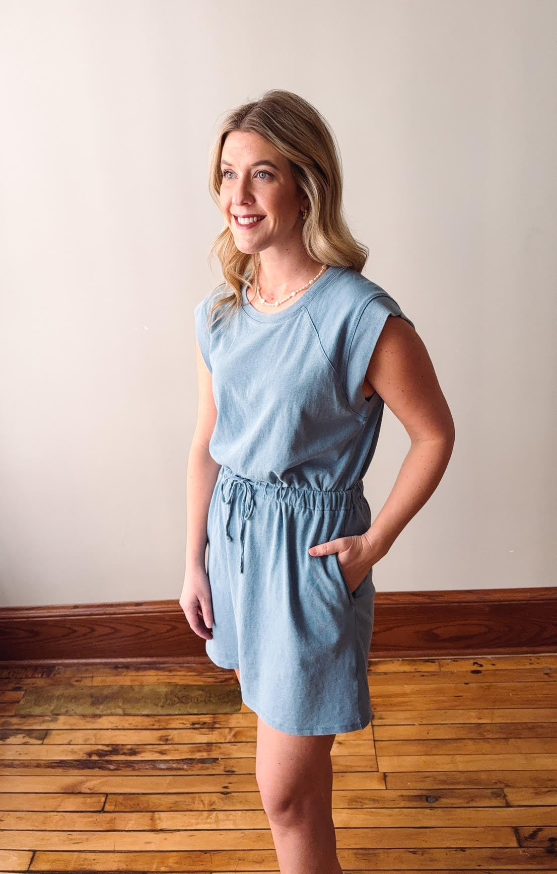 Woman wearing a light blue dress standing on a wooden floor with a white wall background