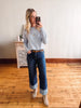 Woman taking a mirror selfie wearing a light blue sweater and blue jeans in a room with wooden flooring.