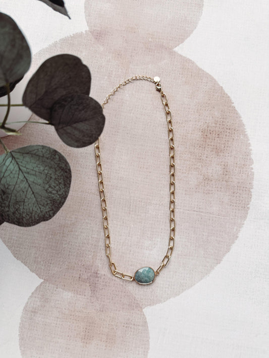Gold chain necklace with a green gemstone pendant on a floral background