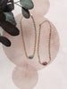 Gold chain necklace with gemstones on a textured beige background