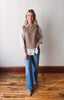 Woman wearing a beige vest over a white shirt with blue jeans on a wooden floor.