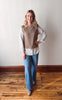 Woman wearing a brown sweater vest over a white shirt with blue jeans on a wooden floor.