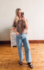 Woman taking a mirror selfie wearing a brown top and blue jeans in a room with wooden flooring.