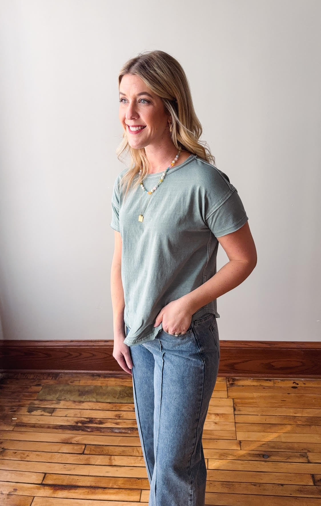 Woman wearing a light green t-shirt and blue jeans standing on a wooden floor.